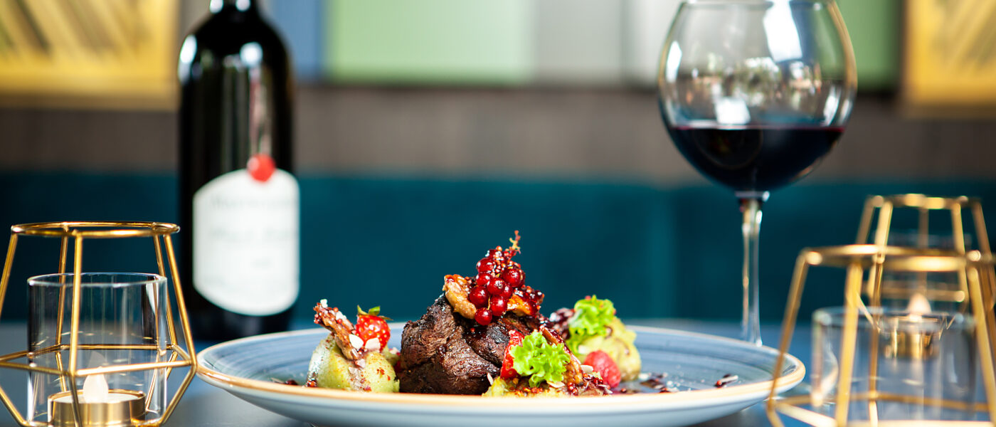 Plat gastronomique dressé avec un magret de canard et un verre de vin rouge, dans un restaurant feutré, sans personne visible