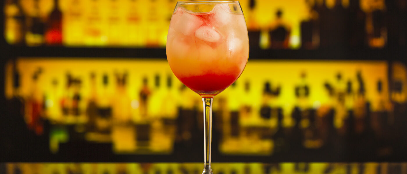 Gros plan sur un cocktail avec glaçons servi au comptoir d'un bar, bouteilles en arrière-plan.
