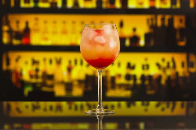 Gros plan sur un cocktail avec glaçons servi au comptoir d'un bar, bouteilles en arrière-plan.