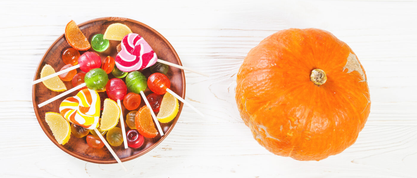 Une citrouille décorative posée près d'une assiette de bonbons et chocolats d'Halloween colorés.