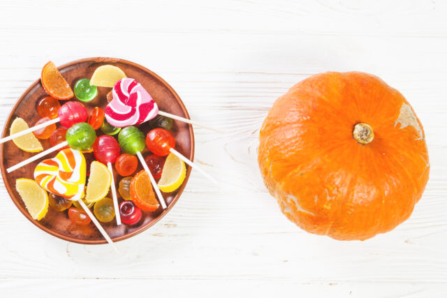 Une citrouille décorative posée près d'une assiette de bonbons et chocolats d'Halloween colorés.
